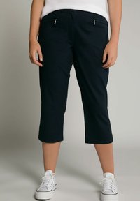 Marineblauwe cropped broek met een gladde textuur, voorzien van ritszakken en een rechte snit, gecombineerd met witte sneakers.