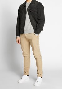 Svart denimjacka, grå sweatshirt, tan chinos, vita sneakers. Anmärkningsvärda detaljer: framfickor, randiga manschetter och klassisk siluett.