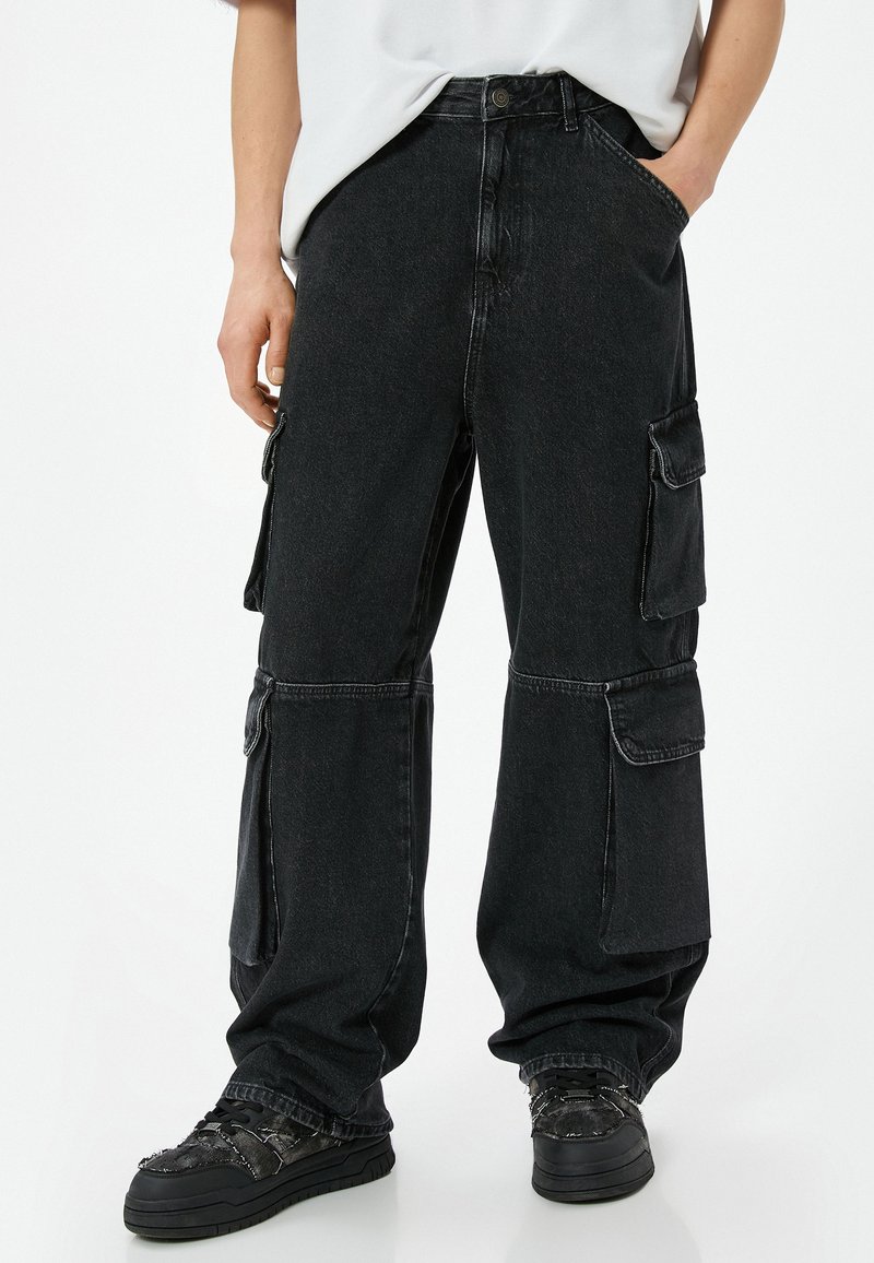 Pantalones cargo de mezclilla negra con un corte relajado, que cuentan con múltiples bolsillos laterales, costuras visibles y una textura ligeramente deslavada.