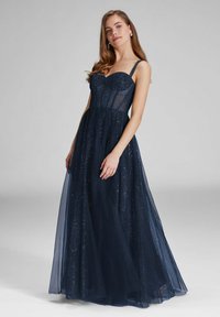 Robe de soirée bleu marine avec un corsage ajusté, un voile transparent et une texture légèrement scintillante. Elle comporte des fines bretelles et une jupe fluide jusqu'au sol.