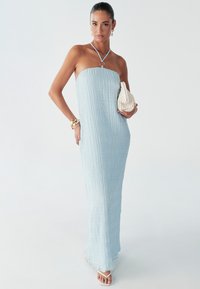 Svetlo modra, brez naramnic maxi obleka iz teksturirane tkanine, oprijetim zgornjim delom in tekočo krilasto ploščo. Srebrn obroč kot poudarek na vratnem delu na traku. Bela torbica.