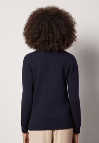 Granatowy sweter z długimi rękawami, okrągłym dekoltem i luźnym krojem. Tkany materiał o fakturowanej powierzchni z gładkim wykończeniem. Bez widocznych wzorów ani akcentów.