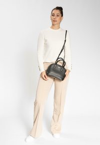 Borsa a tracolla nera in pelle con finitura texturizzata, design arrotondato, doppi manici e tracolla regolabile, tenuta da una persona che indossa una maglietta bianca e pantaloni beige.