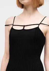 Μαύρο αμάνικο φόρεμα με ραβδωτή υφή, με λεπτές τιράντες και διασταύρωση στο ντεκολτέ. Το ύφασμα φαίνεται μαλακό και ελαστικό.