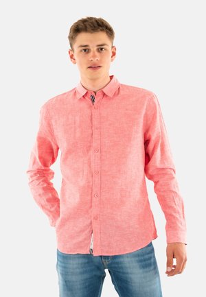 Rosa langärmliges Hemd mit Knopfleiste aus strukturiertem Stoff, mit Kentkragen und einem kontrastierenden Streifendetail am Hals. Kombiniert mit blauen Jeans.