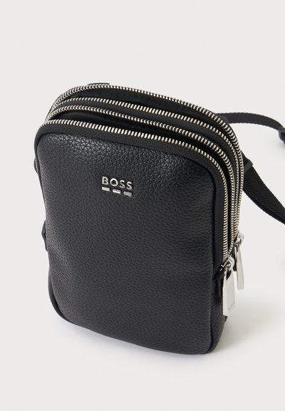 Sac bandoulière en cuir noir texturé avec deux fermetures éclair argentées et logo BOSS à l'avant, présenté sur fond blanc.