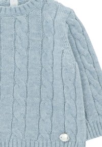 Suéter de punto cableado azul claro con cuello redondo y puños acanalados, con un detalle de botón plateado en el lateral.