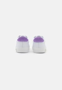 Sneakers bianchi con accenti di pelle scamosciata viola sul tallone e suole in gomma testurizzata, caratterizzati da un design pulito e forma arrotondata, visti da dietro.