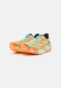Par de zapatillas de running de colores brillantes con patrones en naranja, verde menta y amarillo, y forro negro sobre un fondo blanco.