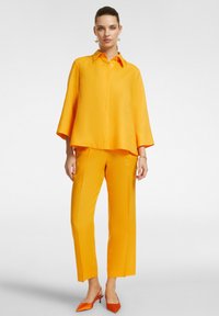 Bright orange two-piece outfit featuring a loose-fit, collared shirt and straight-leg pants, both with a smooth texture and minimal detailing.