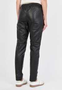Svarta läderbyxor med slim fit, elastisk midja och en slät, matt yta. Har minimal sömnad och tapered ben-design.