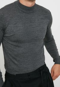 Grauer Strickpullover mit langen Ärmeln und hohem Kragen, glatter Textur und taillierter Passform. Akzentuiert mit gerippten Details am Kragen.