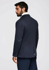Blazer azul marino con solapa muesca, abertura simple y cierre de tres botones. Presenta un cuello interior blanco texturizado y pantalones a juego.