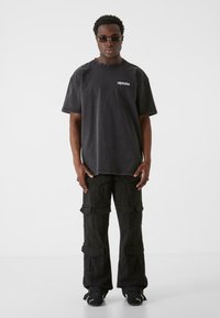 Overdimensioneret sort denim t-shirt med et lille logo og korte ærmer, parret med sorte cargo bukser med flere lommer og en løs pasform.