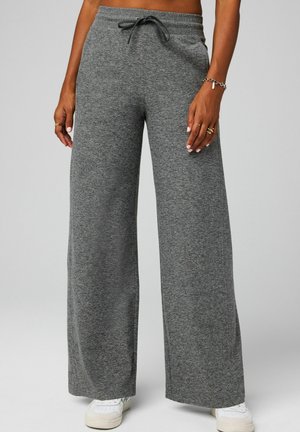 Woman wearing gray wide-leg sweatpants with drawstring waist and white sneakers, standing against a plain background.