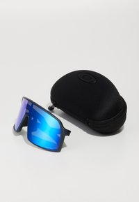 Große schwarze Sonnenbrille mit blauen spiegelnden Gläsern, die ein elegantes, kantiges Design aufweist. Enthält ein schwarzes Hartschalenetui mit Reißverschluss.