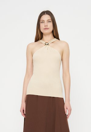 Žena v béžovom tielkovom halter top s detailom zlatého krúžku a hnedej sukni, čelom k prednej strane na bielom pozadí.