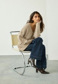 Beige striktrøje med V-hals, brede ærmer, parret med mørke denim flared bukser og brune sko med krokodille-embossed hæle.