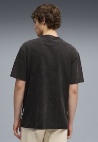 Tricou din bumbac negru, supradimensionat, cu mâneci scurte, guler rotund și o textură ușor estompată. Prezintă un etichetă vizibilă pe cusătura laterală.