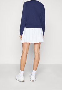 Námornícký svetr s kulatým výstřihem, v kombinaci s bílou plisovanou sukní. Model má na sobě bílé tenisky a ponožky. Hladký povrch látky, volný střih.