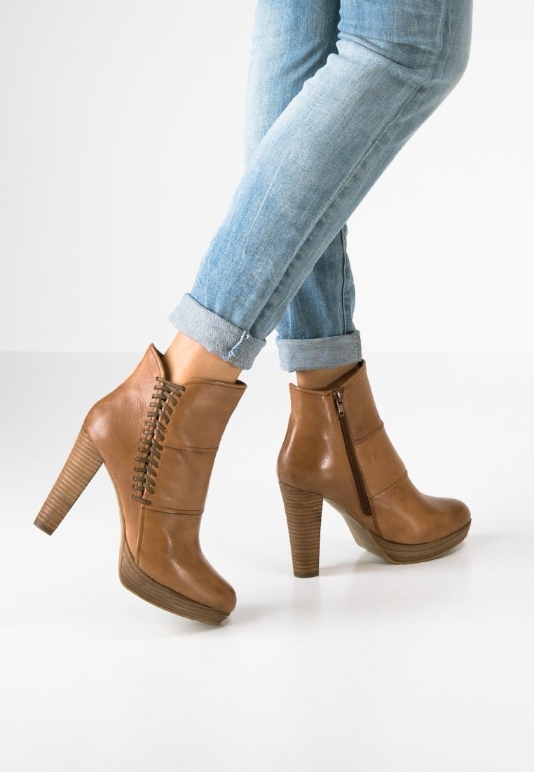 Bottes chevilles en cuir marron avec un talon en coin, dotées d'une fermeture éclair latérale et de coutures décoratives sur le devant. Talon en bois à deux tons.