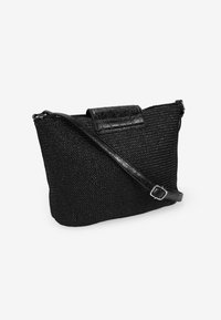 Bolso de mano tejido negro con un cuerpo texturizado, solapa de cuero suave y correa ajustable. Forma compacta con toques mínimos de hardware.