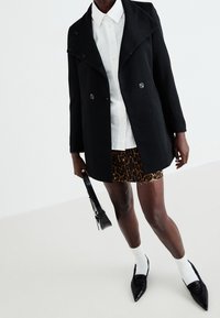 Černý kabát z vlněné směsi s šálovým límcem, dvouřadovým zapínáním, v kombinaci s bílou košilí, sukní s leopardím potiskem a černými botami.