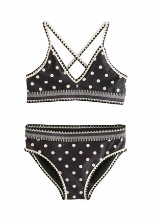 Set bikini nero con pois bianchi, bordatura a zigzag e fascia a righe in vita; il top ha spalline incrociate.