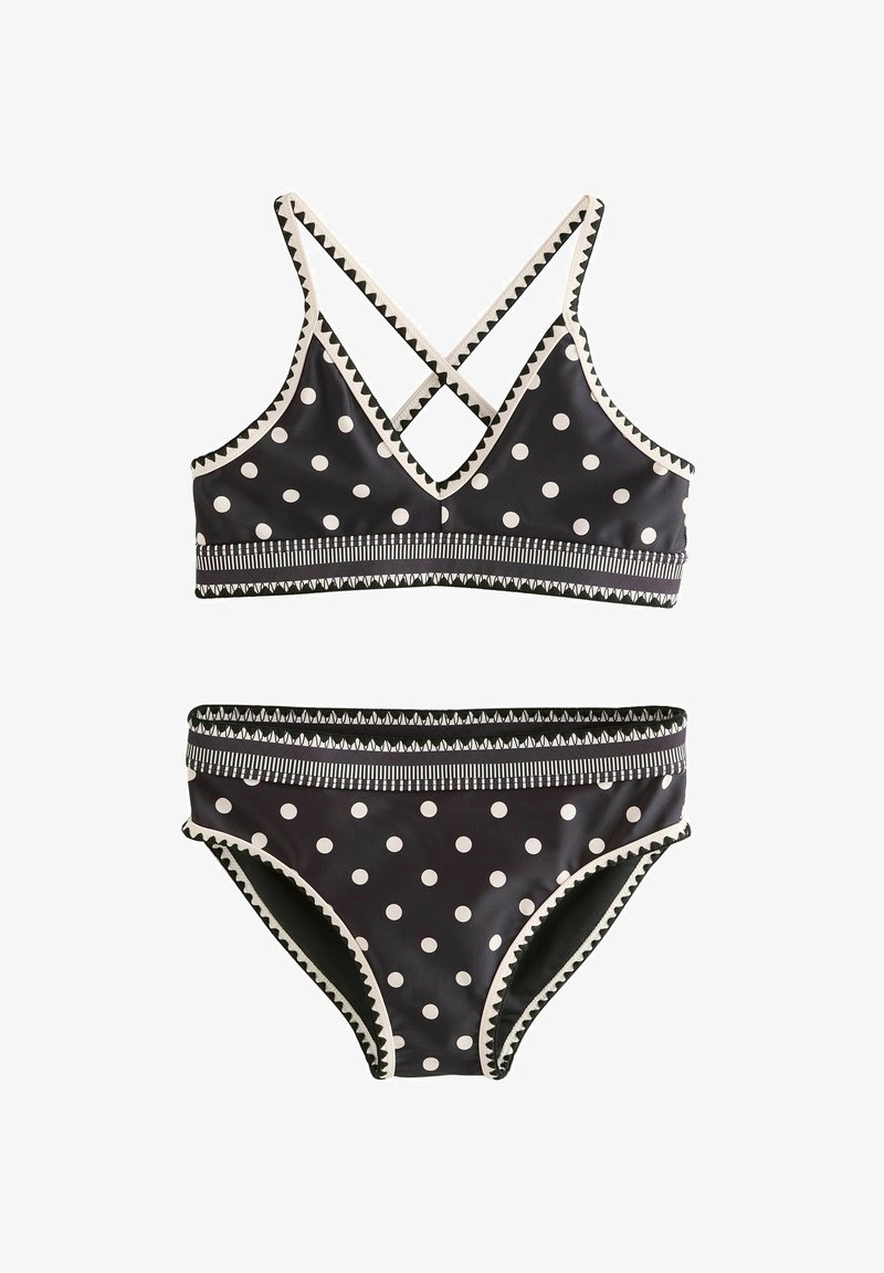 Ensemble bikini noir à pois blancs, bordure en zigzag et ceinture rayée ; le haut possède des bretelles croisées sur les épaules.