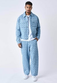 Giacca in denim blu e pantaloni con un motivo geometrico, caratterizzati da una vestibilità ampia, grandi tasche e sneakers bianche. Tessuto texturizzato.