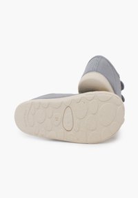 Chaussure en tissu gris avec un bout arrondi, un dessus doux et une semelle extérieure en caoutchouc texturé présentant des motifs circulaires et un logo en relief.