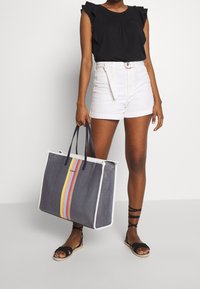 Duża torba na zakupy w kolorze granatowym z białymi wykończeniami, ozdobiona pionowymi paskami w kolorach żółtym, czerwonym i pomarańczowym. Materiał jest tkaniną plecioną, z solidnymi uchwytami.