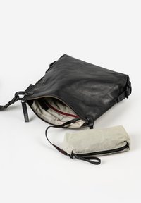 Schwarze Leder-Umhängetasche mit gestreiftem Stofffutter und einer kleinen beigen Reißverschlusstasche daran, auf einer weißen Oberfläche.