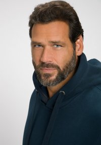 Felpa con cappuccio blu navy con colletto a costine, lacci e un tessuto texturizzato; presenta un primo piano di un uomo con barba.