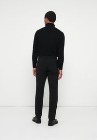 Črn pleten turtleneck pulover v kombinaciji s krojenimi črnimi hlačami. Ima prilagojen dizajn in gladko teksturo z minimalističnimi akcenti.
