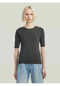 Tricou ajustat de culoare gri închis, cu mâneci scurte, textură striată și detalii de cusătură în contrast, asociat cu blugi de culoare albastru deschis.