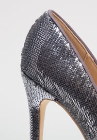 Högklackad sko med ett glittrande överdel i silver och svart paljett, spetsig tådesign och en mjuk beige insida.