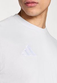 Λευκό βαμβακερό μπλουζάκι με κοντά μανίκια, με διακριτικό λευκό κεντητό λογότυπο τριών ρίγων στο αριστερό στήθος. Λείο ύφασμα.