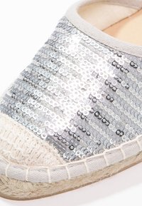 Espadrille argentée à sequins avec une tige en tissu texturé, une bordure en coton beige, une semelle en jute et un design à bout arrondi.