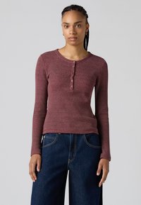 Maglietta henley a maniche lunghe con righe rosse e bianche, colletto rotondo e bottoni a tre, abbinata a jeans larghi blu scuro.