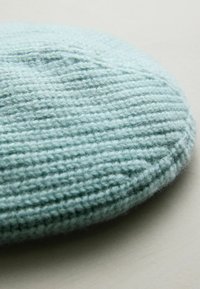 Gebreide ronde kussen in lichtblauwe wol, met een gestructureerd ribbelpatroon en een zachte, donzige oppervlakte voor comfort.