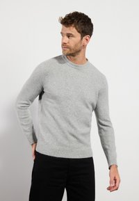 Gray knit sweater with a ribbed crew neckline and cuffs, featuring a smooth texture. Worn with black pants, set against a white background.