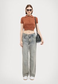 Brun cropped polo shirts med knapper, lyseblå vide jeans, hvite sneakers og en svart skulderveske. Mørke solbriller fullfører looken.
