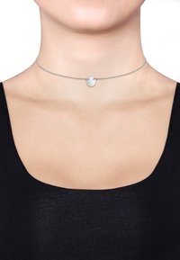 Sølv choker halskæde med en tekstureret cirkulær vedhæng, der har en fin kæde og glat overflade, iført over en mørk top.