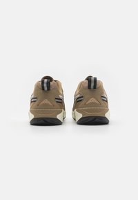 Ruskeat urheilukengät, joissa on teksturoitu päällinen, kontrastiväriset mustat ja valkoiset yksityiskohdat sekä paksu kumipohja, jossa on kuvioitu pito.