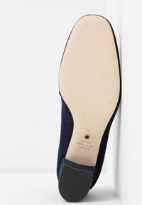 Chaussure en cuir suédé bleu marine avec semelle en cuir et talon noir, affichant la taille 37 et la marque "Stuart Weitzman Fabriqué en Espagne".