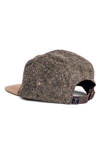 Brown tweed cap with a light brown, flat brim, textured fabric, adjustable strap at the back, and a small logo tag on the side.