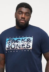Mørkeblå bomulds T-shirt med et grafisk print, der viser palmetræer og skyline, samt teksten "Authentic Jack & Jones" og "Since 1990" fremtrædende vist.
