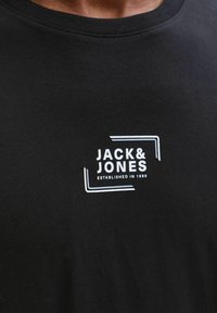 Czarna bawełniana koszulka z białym logo z napisem "JACK & JONES" oraz "ESTABLISHED IN 1990" w prostokątnym wzorze na piersi.