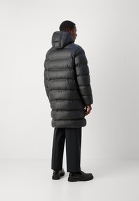 Zwarte gewatteerde pufferjas met capuchon, voorzien van een lange snit en horizontaal gestikte secties. Gekocht met zwarte broeken en schoenen.